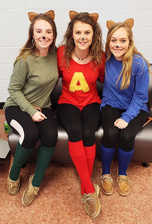 Three students sitting on a couch, dressed in feline Halloween costumes