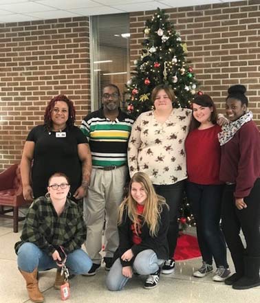 Several students lined up for a photograph in the college lobby, in front of a Christmas tree
