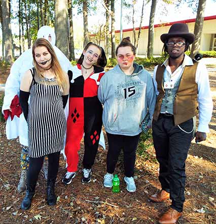 Four students standing outside college buildings, dressed in various Halloween costumes